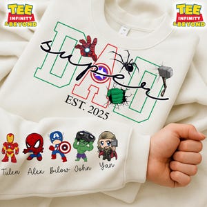Può includere: Felpa bianca con una grafica "Super Papà" verde, rossa e bianca con vari personaggi di supereroi. Il testo "EST. 2025" è sotto la grafica. Cinque piccoli personaggi di supereroi si trovano nella parte inferiore della felpa con i nomi Tulen, Alex, Bilow, John e Yan.