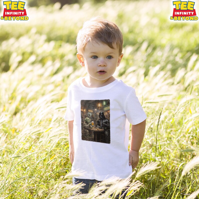 K&ouml;nnte beinhalten: Ein wei&szlig;es T-Shirt mit einem Aufdruck von Darth Vader und Yoda in einer Barszene. Das T-Shirt wird von einem kleinen Kind in einem Feld mit hohem Gras getragen. Das Logo "TEE INFINITY & BEYOND" ist oben links zu sehen.