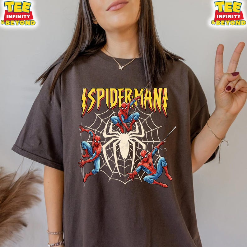 May include: Dark brown t-shirt featuring a Spider-Man graphic. The design includes the word "SPIDERMAN" in yellow lightning bolt font, with Spider-Man figures in red and blue, and a white spiderweb.