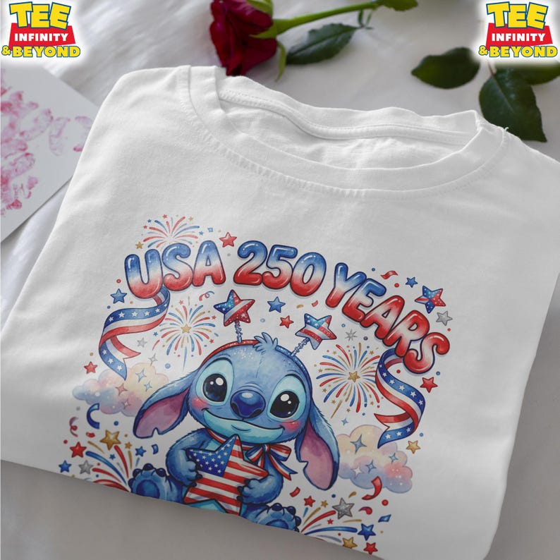 May include: White t-shirt featuring a blue cartoon character holding a star-shaped American flag. The shirt has the text "USA 250 YEARS" in red and blue, with fireworks and star accents, celebrating a patriotic theme.