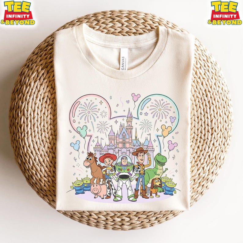 May include: Cream-colored t-shirt featuring a colorful illustration of Disney's Toy Story characters in front of a castle. The design includes fireworks, balloons, and the text "TEE INFINITY & BEYOND" in yellow and orange.