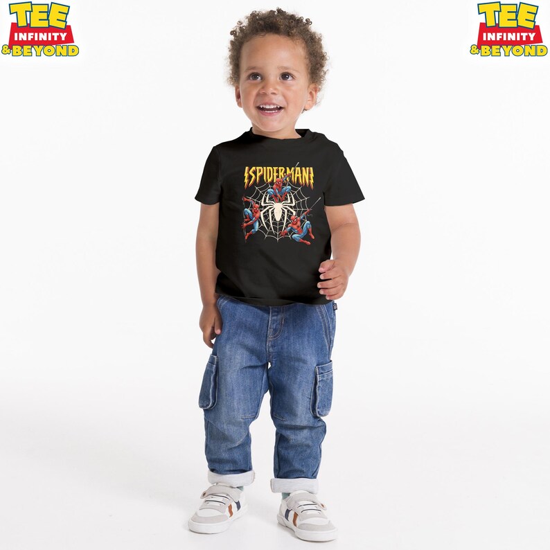 May include: A black Spider-Man t-shirt with a graphic of Spider-Man in a web. The shirt has the text "SPIDERMAN" in yellow. The child is wearing blue jeans and white sneakers.
