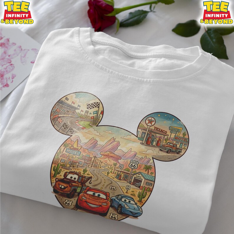 May include: White t-shirt featuring a colorful graphic of a cartoon landscape with race cars, a racetrack, and Route 66 imagery. The design is shaped like Mickey Mouse ears. The shirt has the text "TEE INFINITY & BEYOND" on the top right and left.