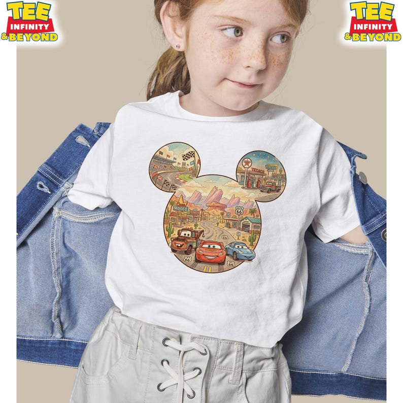 May include: White t-shirt featuring a colorful graphic of Disney's Cars characters within a Mickey Mouse head shape. The design includes images of race tracks, buildings, and the Route 66 sign. The shirt has the text "TEE INFINITY & BEYOND" on the top left and right.