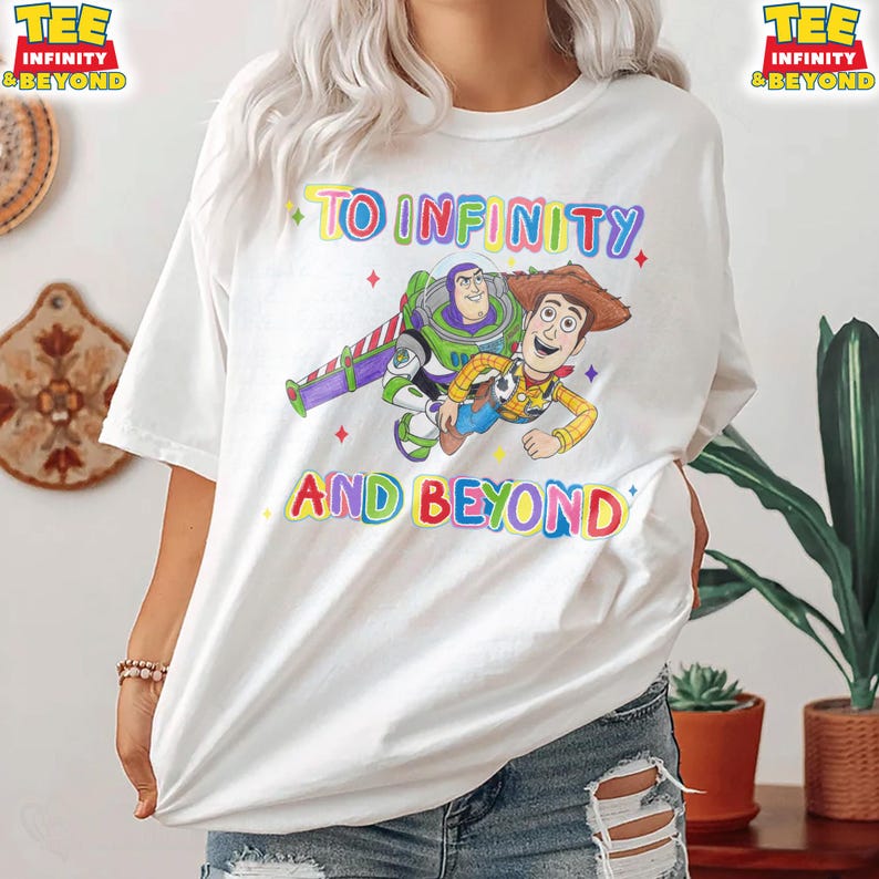 May include: White t-shirt with a colourful graphic of Buzz Lightyear and Woody from Toy Story, and the words "TO INFINITY AND BEYOND". The tee has a crew neck and short sleeves.