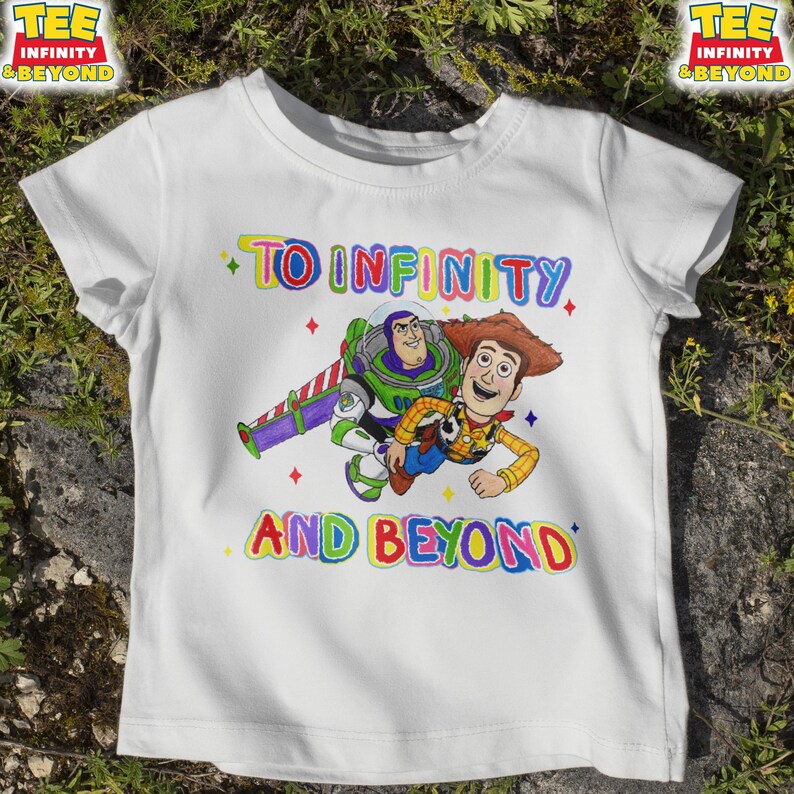 May include: White t-shirt with a colourful graphic of Buzz Lightyear and Woody from Toy Story. The text "TO INFINITY AND BEYOND" is written above and below the characters in rainbow colours. The shirt has short sleeves.