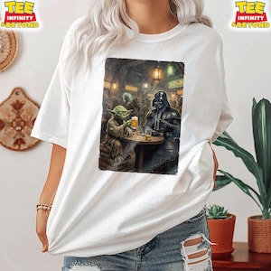 K&ouml;nnte beinhalten: Wei&szlig;es T-Shirt mit einer humorvollen Illustration von Yoda und Darth Vader in einer Bar, beide mit einem Bier. Das Bild hat eine Vintage-&Auml;sthetik. Das Shirt hat den Text "TEE INFINITY & BEYOND" oben rechts und links.