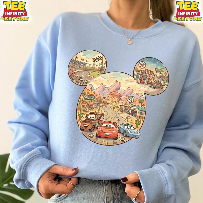 May include: Light blue sweatshirt featuring a Mickey Mouse head design with a Cars theme. The design includes a race track, desert landscape, and Route 66 elements. The sweatshirt has the text "TEE INFINITY & BEYOND" on the top left and right.