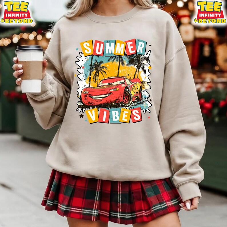 May include: Beige sweatshirt with a graphic of a red race car with the text "SUMMER VIBES". The design includes palm trees and a colorful border. The sweatshirt is paired with a red and black plaid skirt.