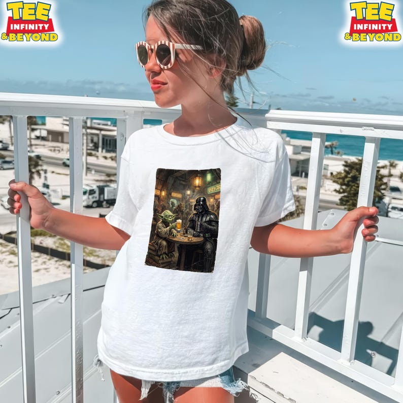K&ouml;nnte beinhalten: Wei&szlig;es T-Shirt mit einem Star Wars-Motiv von Yoda und Darth Vader in einem Pub. Das T-Shirt hat oben den Text "TEE INFINITY & BEYOND". Das Bild ist auf einer Person mit Sonnenbrille, die sich drau&szlig;en aufh&auml;lt.