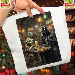 K&ouml;nnte beinhalten: Wei&szlig;es T-Shirt mit einer Star Wars-Illustration. Yoda und Darth Vader sitzen in einer Bar an einem Tisch und halten jeweils ein Bier. Der Hintergrund zeigt eine &uuml;berf&uuml;llte Barszene mit verschiedenen au&szlig;erirdischen Charakteren.