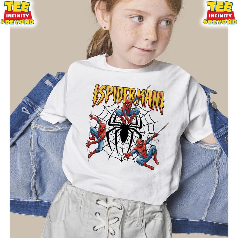 May include: White t-shirt featuring a Spider-Man graphic. The design includes the word "SPIDERMAN" in yellow and red, along with illustrations of Spider-Man and a spider web. The shirt is worn by a person.
