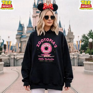Puede incluir: Sudadera negra con un gr&aacute;fico de donut rosa y el texto "ZOOTOPIA'S THE BIG DONUT" y "Cittle Rodentia". La sudadera tiene un bolsillo delantero y una capucha con cord&oacute;n. Un castillo se ve en el fondo.