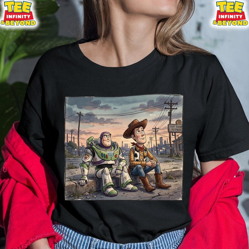 May include: Black t-shirt with a cartoon image of Buzz Lightyear and Woody from Toy Story. They are sitting together with a cityscape backdrop, and the words "Toy Town Repair" are visible.