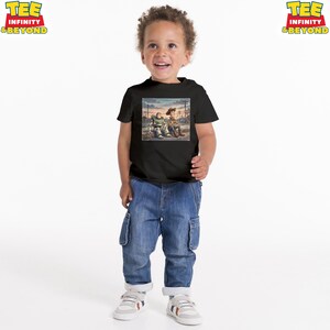 May include: A black t-shirt with a graphic of two animated characters. The characters are sitting together in a scene with a sunset background. The child is wearing blue jeans and white trainers.