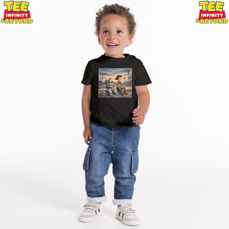 May include: A black t-shirt with a graphic of two animated characters. The characters are sitting together in a scene with a sunset background. The child is wearing blue jeans and white trainers.