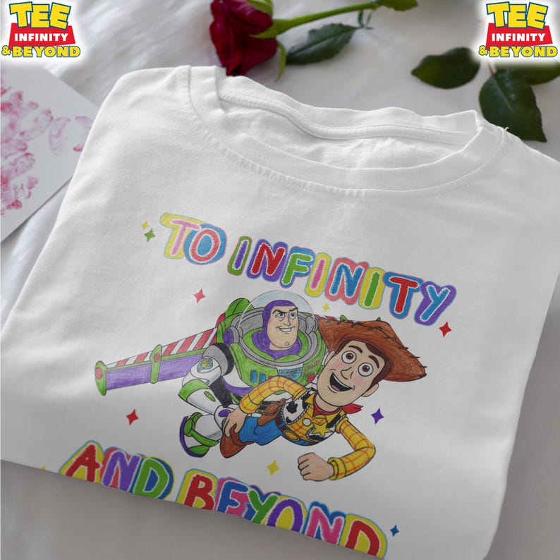 May include: White t-shirt with a colourful graphic of Buzz Lightyear and Woody from Toy Story, and the text "TO INFINITY AND BEYOND" in rainbow colours. The shirt has a crew neck and short sleeves.