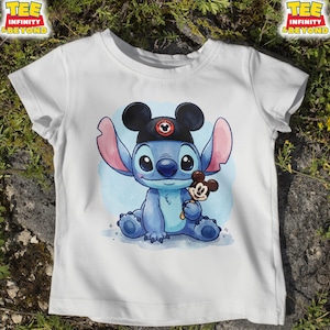 K&ouml;nnte beinhalten: Wei&szlig;es T-Shirt mit einer blauen Cartoonfigur, die einen schwarzen Hut mit Mickey Mouse-Ohren tr&auml;gt und ein Mickey Mouse-Eis h&auml;lt. Das T-Shirt hat den Text "TEE INFINITY & BEYOND" oben links und rechts.