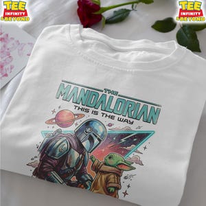 Może przedstawiać: Biały t-shirt z nadrukiem graficznym przedstawiającym Mandalorianina i Grogu. Tekst głosi THE MANDALORIAN THIS IS THE WAY. Wz&oacute;r zawiera planetę z pierścieniami, tr&oacute;jkątną ramkę w stylu neonowym, chmury oraz gwiazdy w odcieniach niebieskiego, r&oacute;żu i brązu.