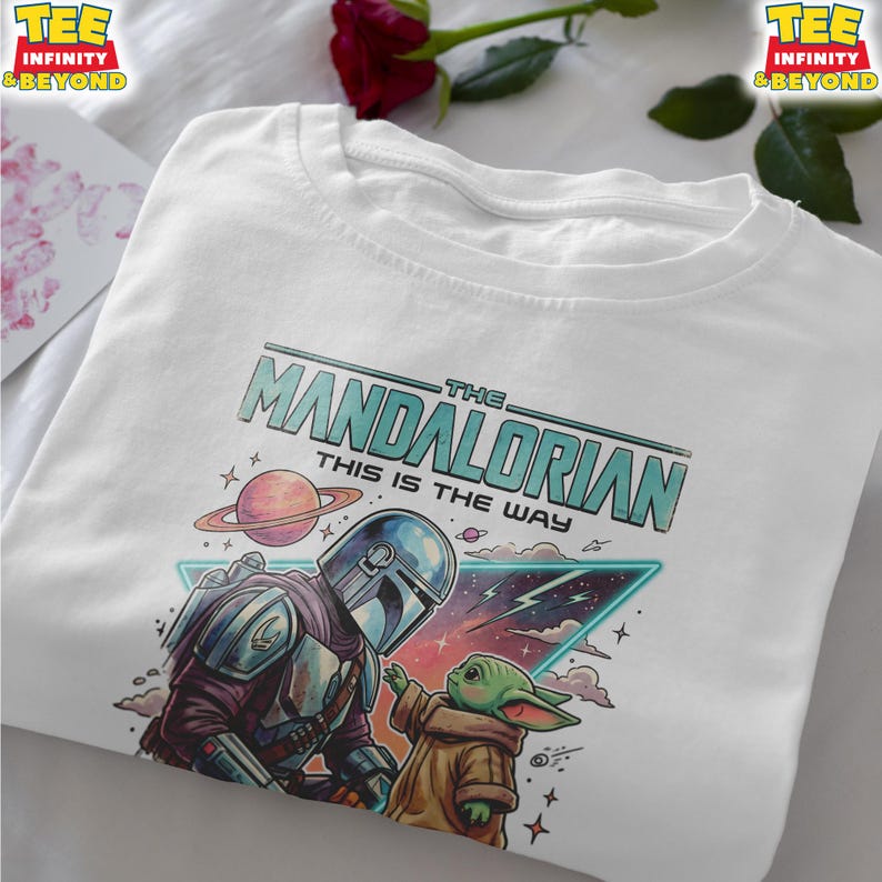 Może przedstawiać: Biały t-shirt z nadrukiem graficznym przedstawiającym Mandalorianina i Grogu. Tekst głosi THE MANDALORIAN THIS IS THE WAY. Wz&oacute;r zawiera planetę z pierścieniami, tr&oacute;jkątną ramkę w stylu neonowym, chmury oraz gwiazdy w odcieniach niebieskiego, r&oacute;żu i brązu.