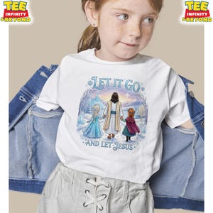 以下が含まれることがあります： 「LET IT GO AND LET JESUS」の文字と、イエスと2人の女の子が冬のシーンにいるイラストが描かれた白いTシャツ。Tシャツはクルーネックで半袖です。Tシャツは人が着ています。
