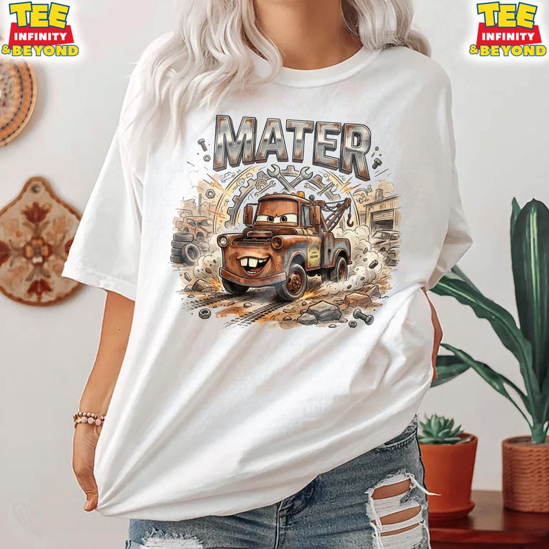 May include: White t-shirt featuring a cartoon illustration of Mater from the Cars movie. The design includes the name "MATER" in a distressed font, along with tools and a tow truck. The shirt has short sleeves and a crew neck.