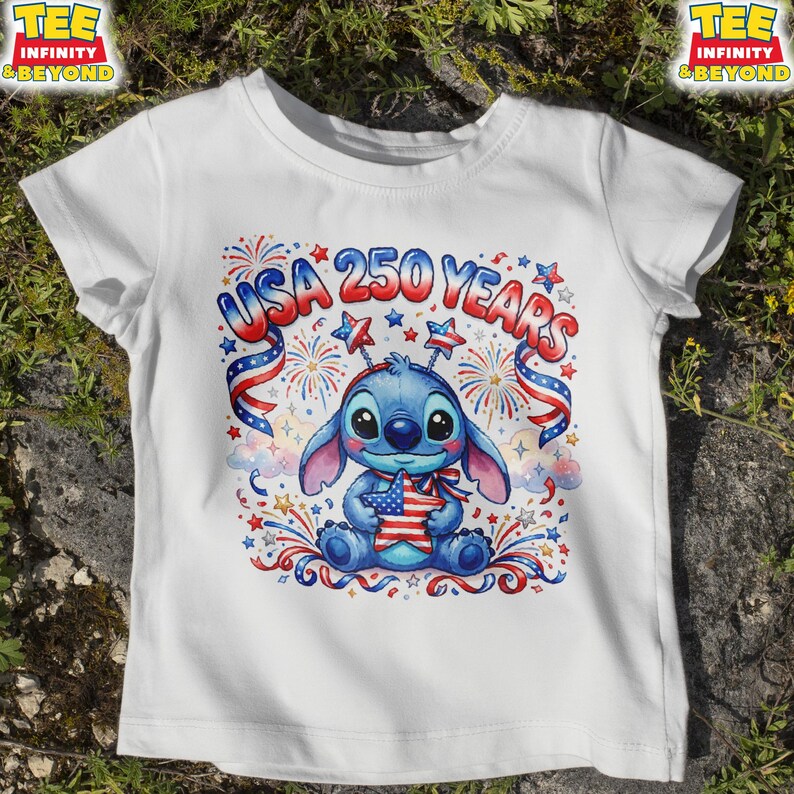 May include: White t-shirt featuring a blue cartoon character holding a star-shaped American flag. The shirt has the text "USA 250 YEARS" in red and blue, with fireworks and star accents. The design is centered on the front of the shirt.