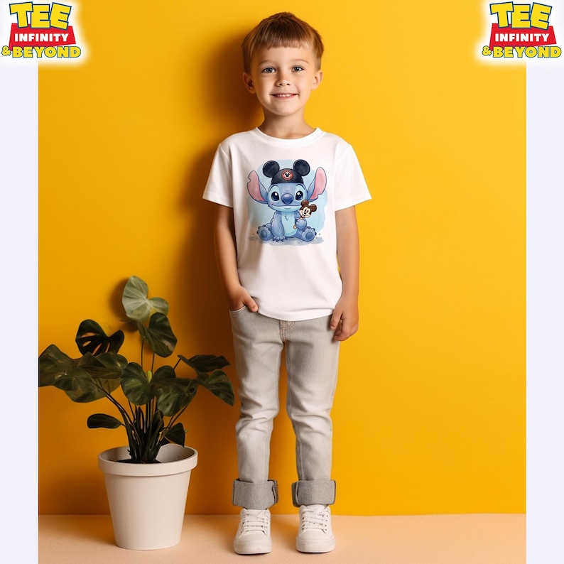 K&ouml;nnte beinhalten: Ein wei&szlig;es T-Shirt mit einem Cartoon-Stitch-Charakter, der einen Mickey-Mouse-Hut tr&auml;gt und ein Mickey-Mouse-Pl&uuml;schtier h&auml;lt. Das T-Shirt wird von einem kleinen Kind getragen. Die Worte "TEE INFINITY & BEYOND" sind oben links und rechts aufgedruckt.