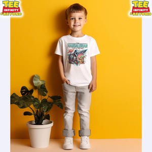 Może przedstawiać: Biały t-shirt z kr&oacute;tkim rękawem z nadrukiem graficznym przedstawiającym Mandalorianina i Grogu oraz napisem "THE MANDALORIAN THIS IS THE WAY" powyżej, na tle o tematyce kosmicznej z kolorowymi planetami i gwiazdami.