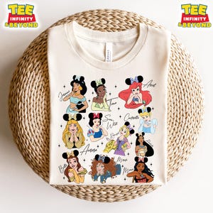 May include: A white t-shirt with a design of 12 Disney princesses with mouse ears. The princesses include Belle, Aurora, Snow White, Cinderella, Ariel, Tiana, Jasmine, Pocahontas, Mulan, Rapunzel, Merida, and Moana.