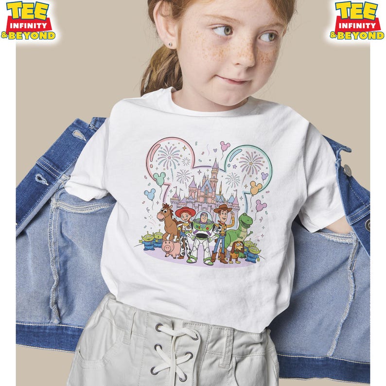 May include: White t-shirt featuring a colorful graphic of Disney's Toy Story characters, including Woody, Buzz Lightyear, and Rex, with a castle and fireworks design. The shirt has the text "TEE INFINITY & BEYOND" at the top.