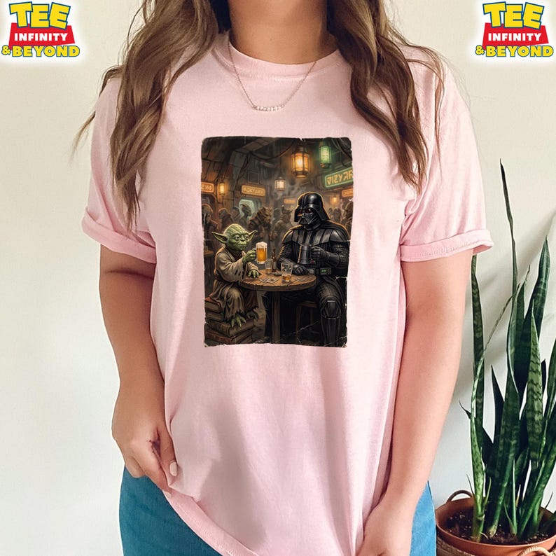 K&ouml;nnte beinhalten: Hellrosa T-Shirt mit einem Star Wars-Motiv. Die Grafik zeigt Yoda und Darth Vader in einer Bar, beide mit einem Bier. Das Shirt hat hochgekrempelte &Auml;rmel und die Worte "TEE INFINITY & BEYOND" sind oben links und rechts aufgedruckt.