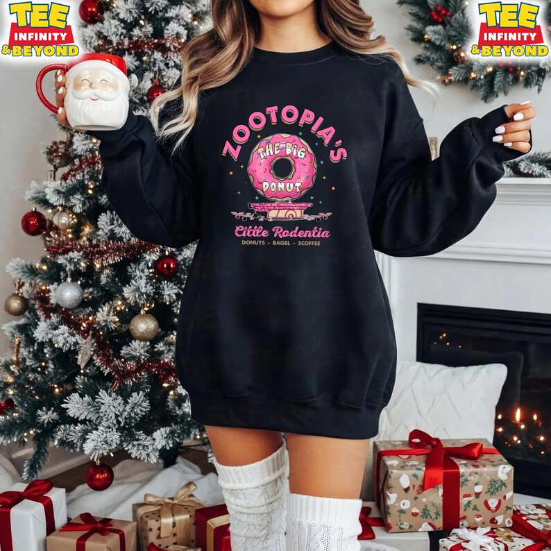 Puede incluir: Sudadera negra con un gr&aacute;fico de donut rosa y el texto "Zootopia's The Big Donut" y "Little Rodentia". La sudadera se combina con calcetines altos blancos. Un &aacute;rbol de Navidad y regalos est&aacute;n en el fondo.