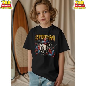 May include: Black t-shirt featuring the word "SPIDERMAN" in yellow and red, with a white spider and web design. The shirt also has illustrations of Spider-Man in action. The shirt is worn by a child.