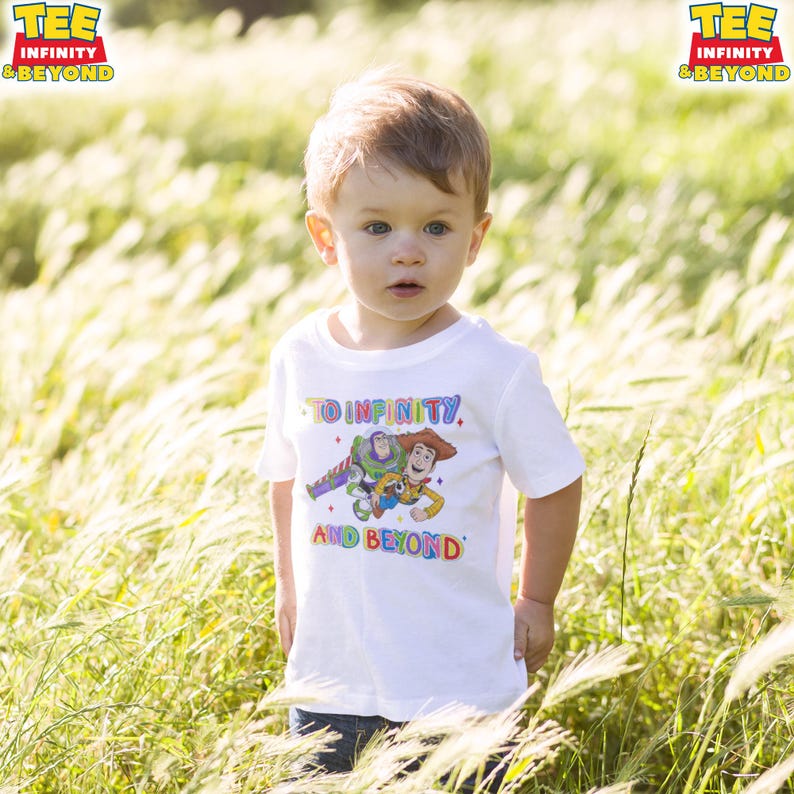May include: A white t-shirt with a colourful graphic of Buzz Lightyear and Woody from Toy Story, and the text "TO INFINITY AND BEYOND." A young child wears the shirt while standing in a field of tall grass. The shirt has the words "TEE INFINITY & BEYOND" on the top left.