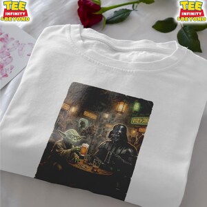 K&ouml;nnte beinhalten: Wei&szlig;es T-Shirt mit einer Grafik von Yoda und Darth Vader in einer Bar, jeder mit einem Bier. Die Grafik hat einen Vintage-Illustrationsstil. Das Shirt hat den Text "TEE INFINITY & BEYOND" oben links und rechts.
