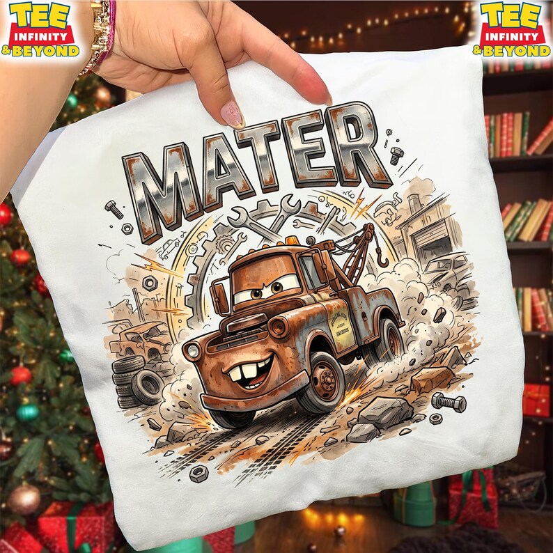 May include: White t-shirt featuring a cartoon illustration of Mater from the movie Cars. The design includes the name "MATER" in large, metallic letters, along with tools, gears, and a garage scene. The image is a detailed, colorful graphic.