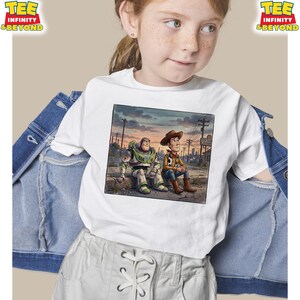 May include: White t-shirt with a graphic of Buzz Lightyear and Woody from Toy Story. The illustration shows them sitting together against a city backdrop. The shirt has the text "TEE INFINITY & BEYOND" in the upper left and right corners.