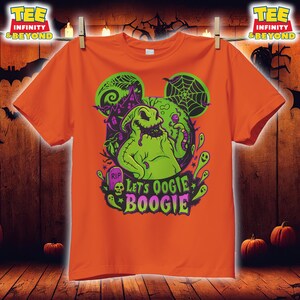 K&ouml;nnte beinhalten: Orangefarbenes T-Shirt mit einem gr&uuml;nen Oogie Boogie-Design, einem Spukhaus und einem Spinnennetz. Der Text "Let's Oogie Boogie" ist in Gr&uuml;n und Lila gehalten. Das T-Shirt h&auml;ngt an einer W&auml;scheleine.