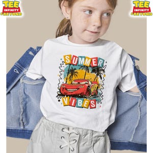 May include: White t-shirt featuring a graphic of a red race car with the text "SUMMER VIBES". The design includes palm trees and a colorful background. The shirt is part of the "TEE INFINITY & BEYOND" collection.