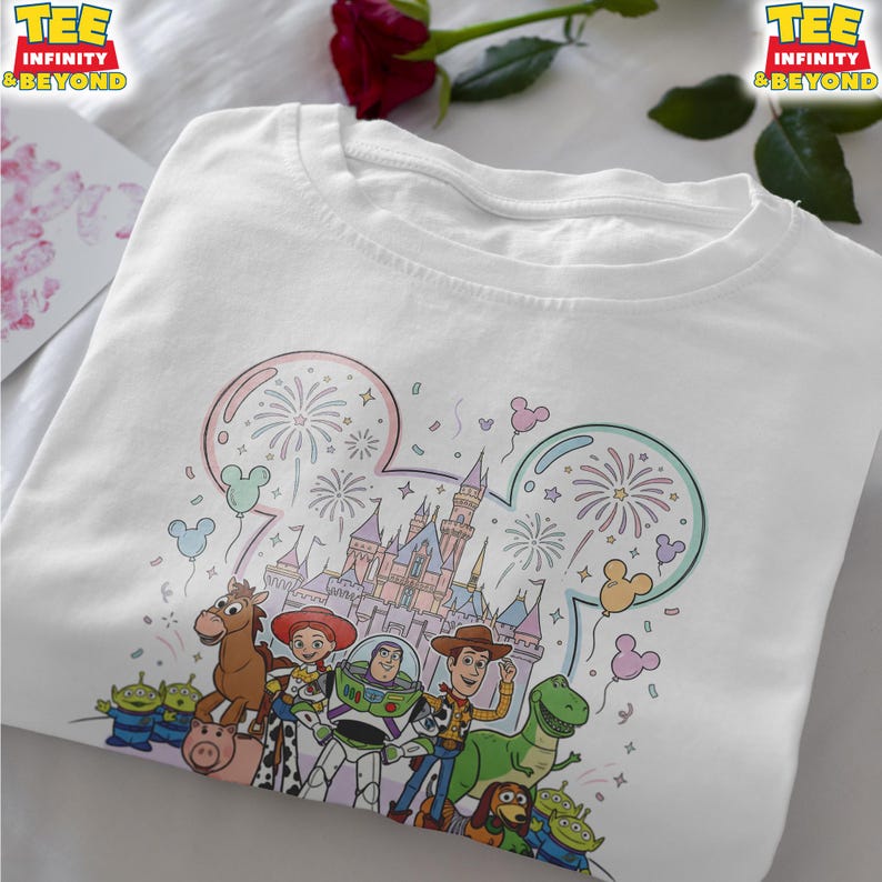 May include: White t-shirt featuring a colorful graphic of Disney characters, including Woody, Buzz Lightyear, and others, in front of a castle with fireworks. The shirt has the text "TEE INFINITY & BEYOND" at the top.