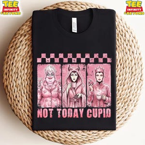 May include: Black t-shirt featuring three pink-toned illustrations of Disney villains. The illustrations are framed by a pink checkered border. The text "NOT TODAY CUPID" is printed in pink below the illustrations. The shirt has a crew neck.