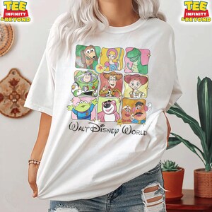 Puede incluir: Camiseta blanca con un dise&ntilde;o de cuadr&iacute;cula colorida de personajes de Toy Story. El texto "Walt Disney World" est&aacute; impreso debajo. La camiseta tiene mangas cortas y un corte holgado.