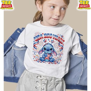 May include: White t-shirt featuring a blue cartoon character holding a star-shaped American flag. The shirt has the text "USA 250 YEARS" in red, white, and blue, with stars and fireworks. The shirt is worn by a child.