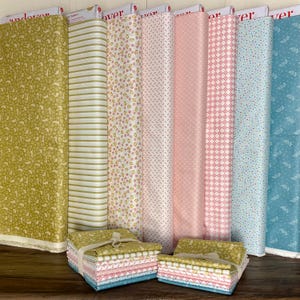 May include: A collection of fabric rolls and folded fabric bundles in various patterns and colors. The rolls include floral, striped, and geometric designs in shades of green, pink, and blue. The folded bundles are tied with twine.