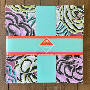 May include: A bundle of fabric squares featuring a floral pattern in shades of purple, green, black, and white. The fabric is wrapped with a turquoise band and an orange and pink stripe. The label reads "Kaffe Fassett Collective".