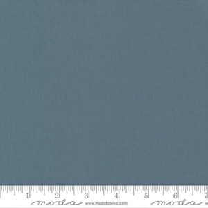 May include: A solid, textured fabric in a muted teal color. The fabric has a subtle grid pattern and is shown with a ruler along the bottom edge, marked in inches. The fabric is likely intended for quilting or other sewing projects.