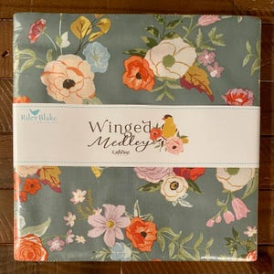 May include: A square fabric bundle featuring a floral design with orange, pink, and white flowers on a teal background. The bundle is wrapped with a white band that reads "Winged Medley" and includes a bird illustration. The brand name "Riley Blake Designs" is also visible.