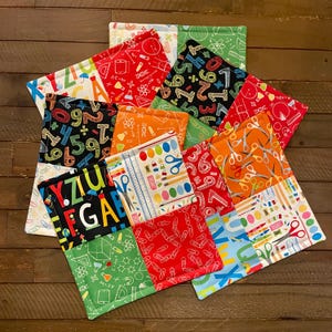 May include: A collection of colorful, square fabric patches with school-themed patterns. Designs include numbers, scissors, pencils, rulers, and other school supplies. The patches are arranged in a circular pattern, showcasing a variety of colors and designs.