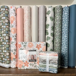 May include: A collection of fabric rolls and a stack of fabric squares. The rolls feature various floral and geometric patterns in shades of green, peach, and blue. A package with a floral design and a photo is in the center.